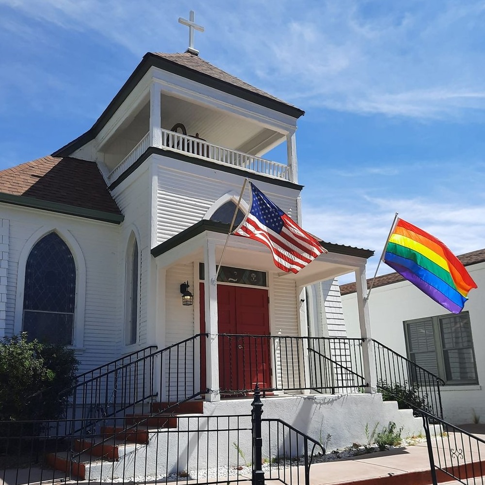 white church building with American and Rainbow flags flying in front